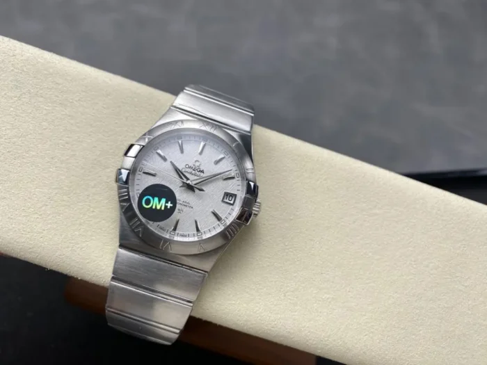 Wider shot of the 38mm textured white model on the cushion with its silver tone bracelet