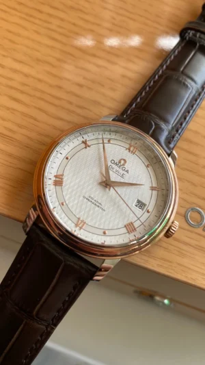 Angled on a wooden box, rose gold tone Roman numerals on a white textured dial