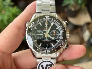 Black chronograph in hand, plants behind