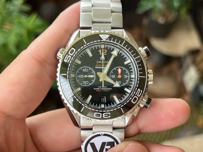 Black chronograph in hand, plants behind
