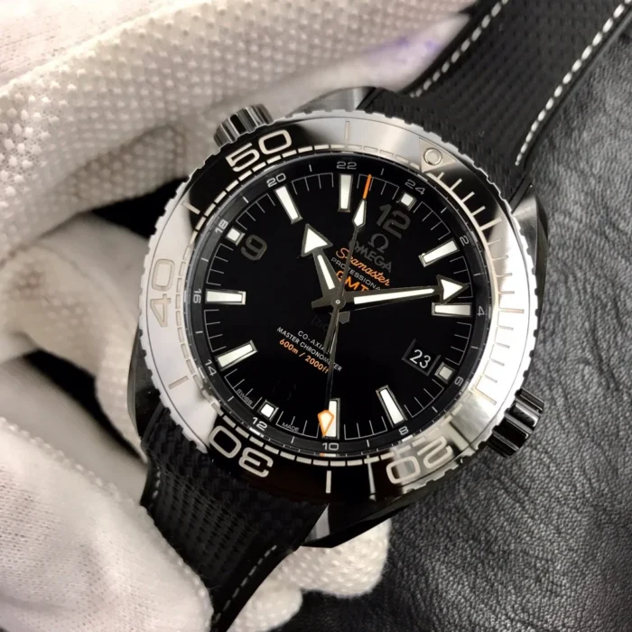 Black GMT dial at an angle in a gloved hand, orange-accent Deep Black GMT