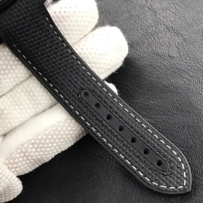 Black strap with white stitching and holes, in a gloved hand