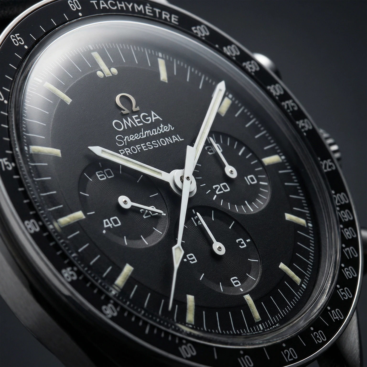 Extreme close-up of an authentic Omega Speedmaster Professional dial filling the frame, captured with an elegant diagonal tilt and subtle rotation.